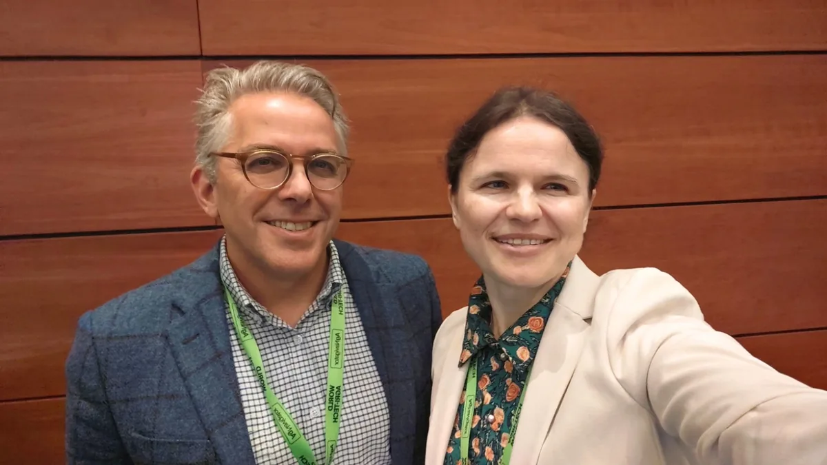 Dr. Maryna Kuzmenko in a selfie with Dr Elliott Grant, in glasses and a checked jacket, in a wood-panelled conference foyer.