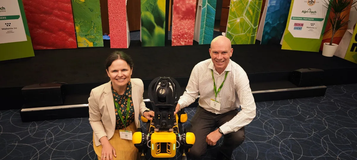 Dr. Maryna Kuzmenko and Rob Lind crouching either side of a yellow Spot quadruped robot on the summit floor, in front of the stage.