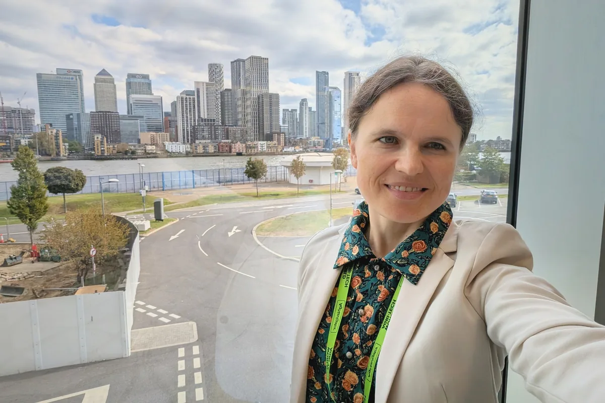 Dr. Maryna Kuzmenko in a selfie at a window, with the Canary Wharf skyline and the river behind her.