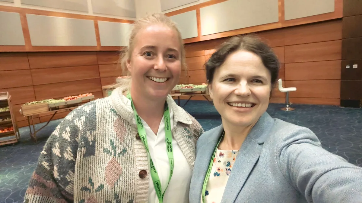 Dr. Maryna Kuzmenko and Chloe Marshall smiling in a selfie in a wood-panelled conference hall, with a buffet table behind them.