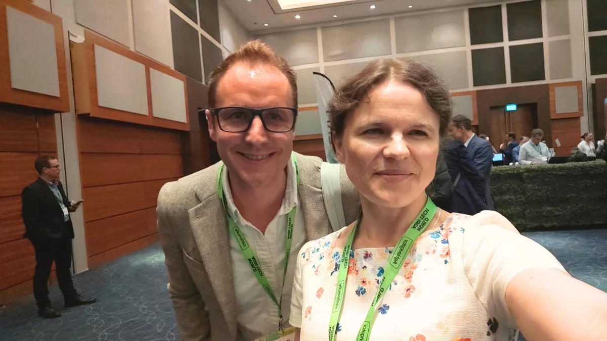 Dr. Maryna Kuzmenko and Mark Jarman, in glasses and a light jacket, in a selfie in the conference foyer with delegates in the background.
