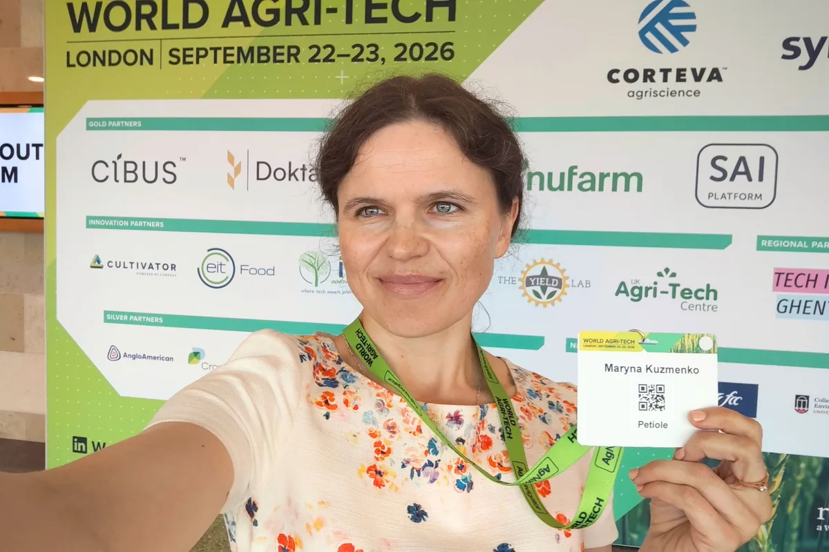 Dr. Maryna Kuzmenko holding up her delegate badge in front of the World Agri-Tech London 2026 partner wall.