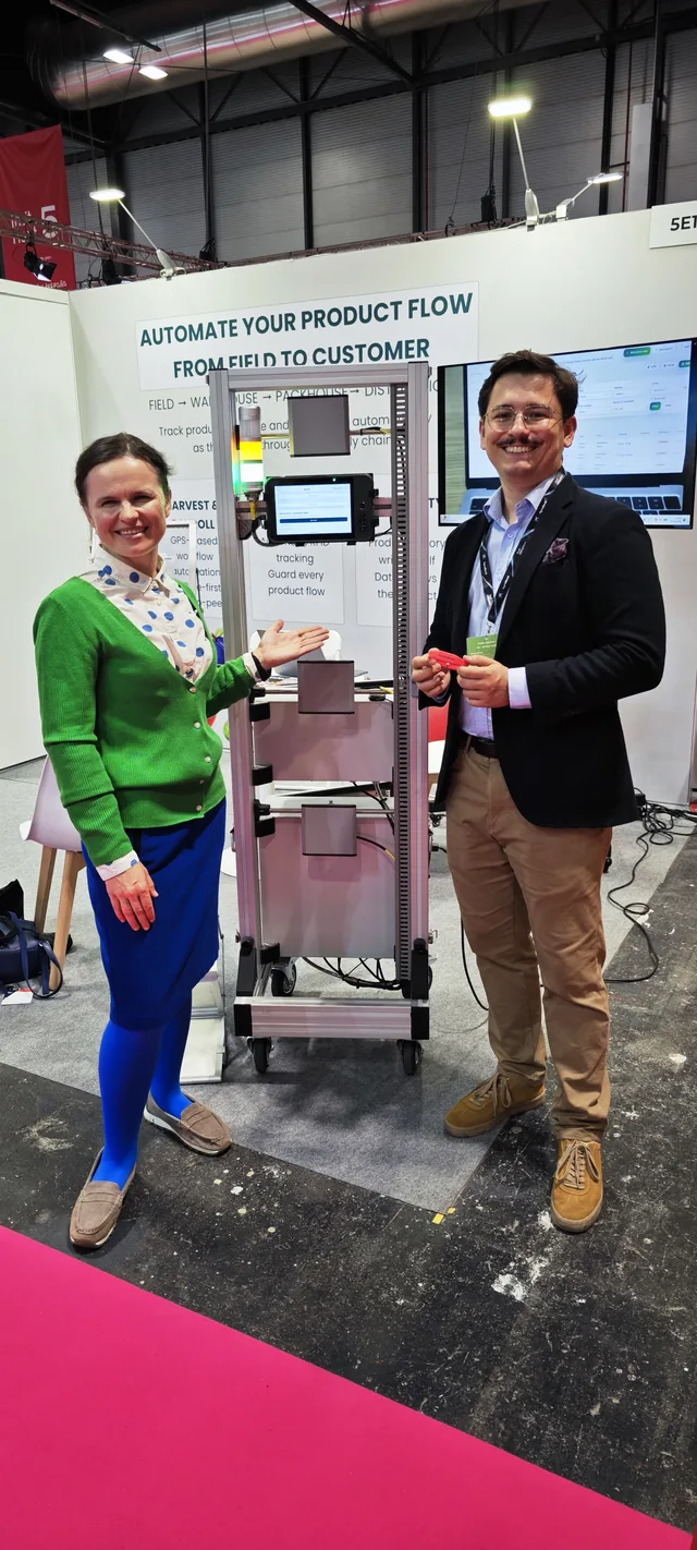 Dr. Maryna Kuzmenko and Kacper Dach standing beside a stand on a pink carpet, with a display screen behind them.