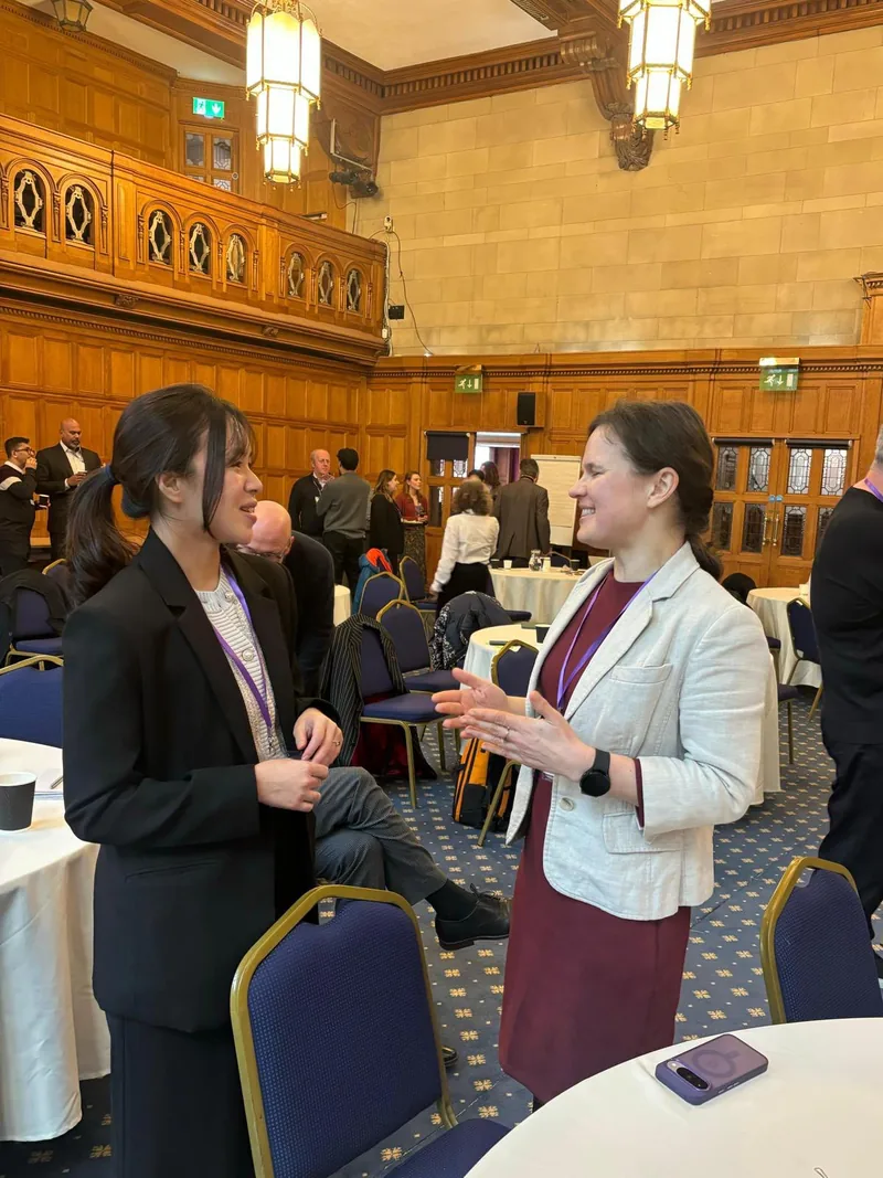 Dr. Maryna Kuzmenko in conversation with another delegate in a wood-panelled hall set with round tables.